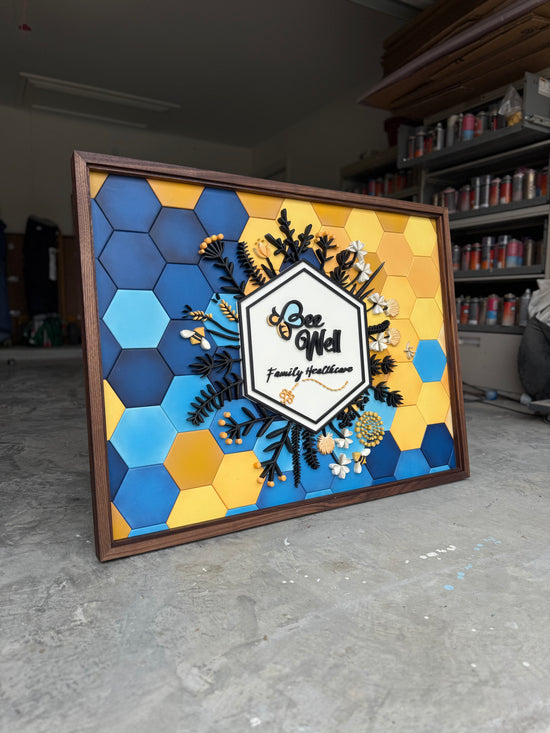 Bee Well Sign with hexagon blue/yellow gradient background, flowers, logo, walnut frame