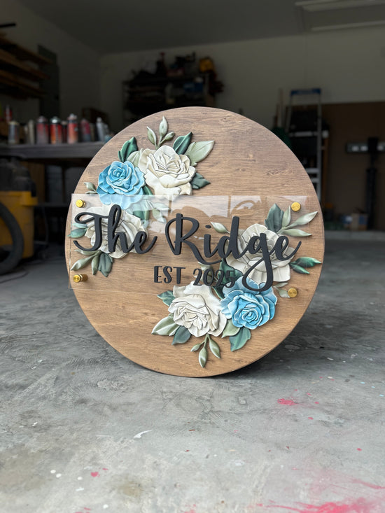 The Ridge wooden sign with white and blue flowers and brown wooden circle