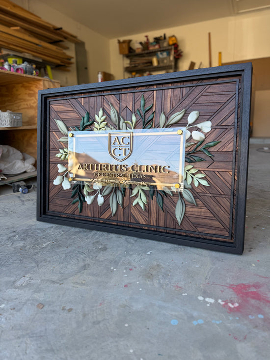ACCT Arthritis Clinic of Central Texas wooden sign with greenery border and walnut pattern. Triple black frame in garage
