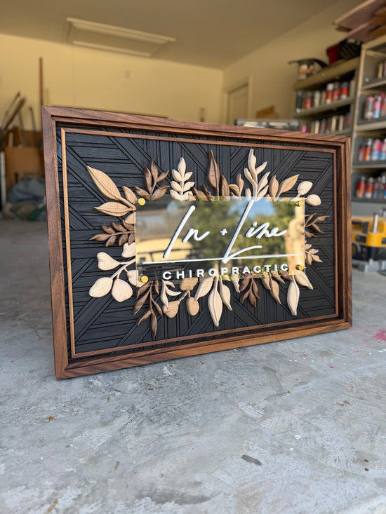 In Line Chiro Logo sign with wooden leaves and a mosaic black patterned background, triple walnut frame on display in garage