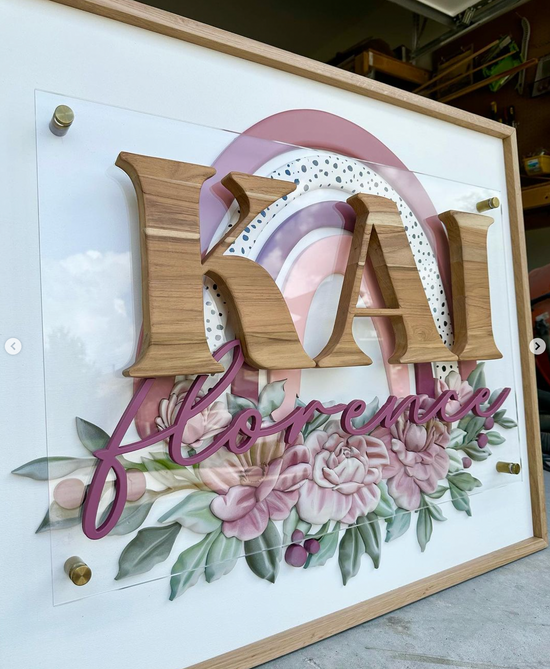 Kai Florence on white backer with wood frame square sign with rainbow and flowers