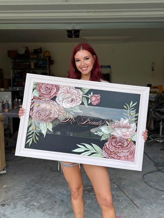 Love me beauty studio logo sign with white frame, black background, pink and green flowers, being held by marissa