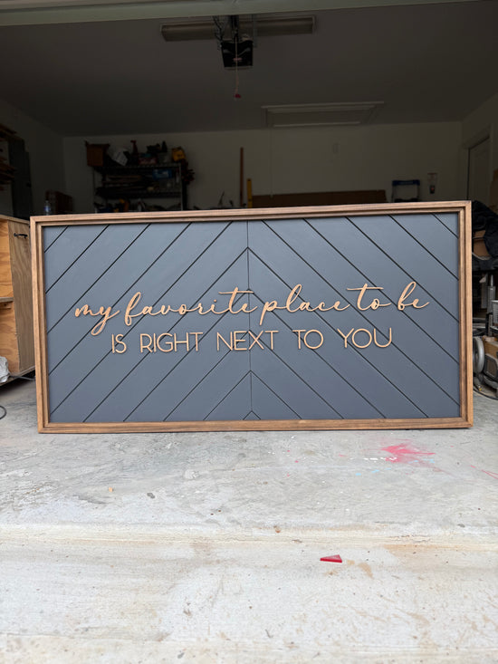 My favorite place to be is right next to you sign with a patterned background and wood frame
