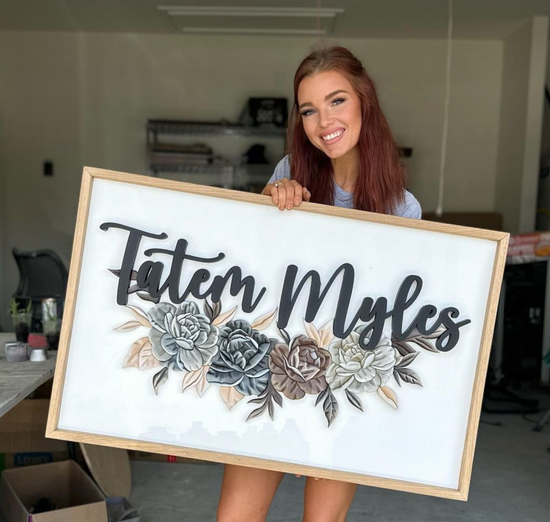 Tatem Myles name on white backer with natural wood frame and flowers under name