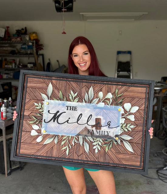 The Miller Family sign on walnut mosaic background with triple black frame, greenery and being held